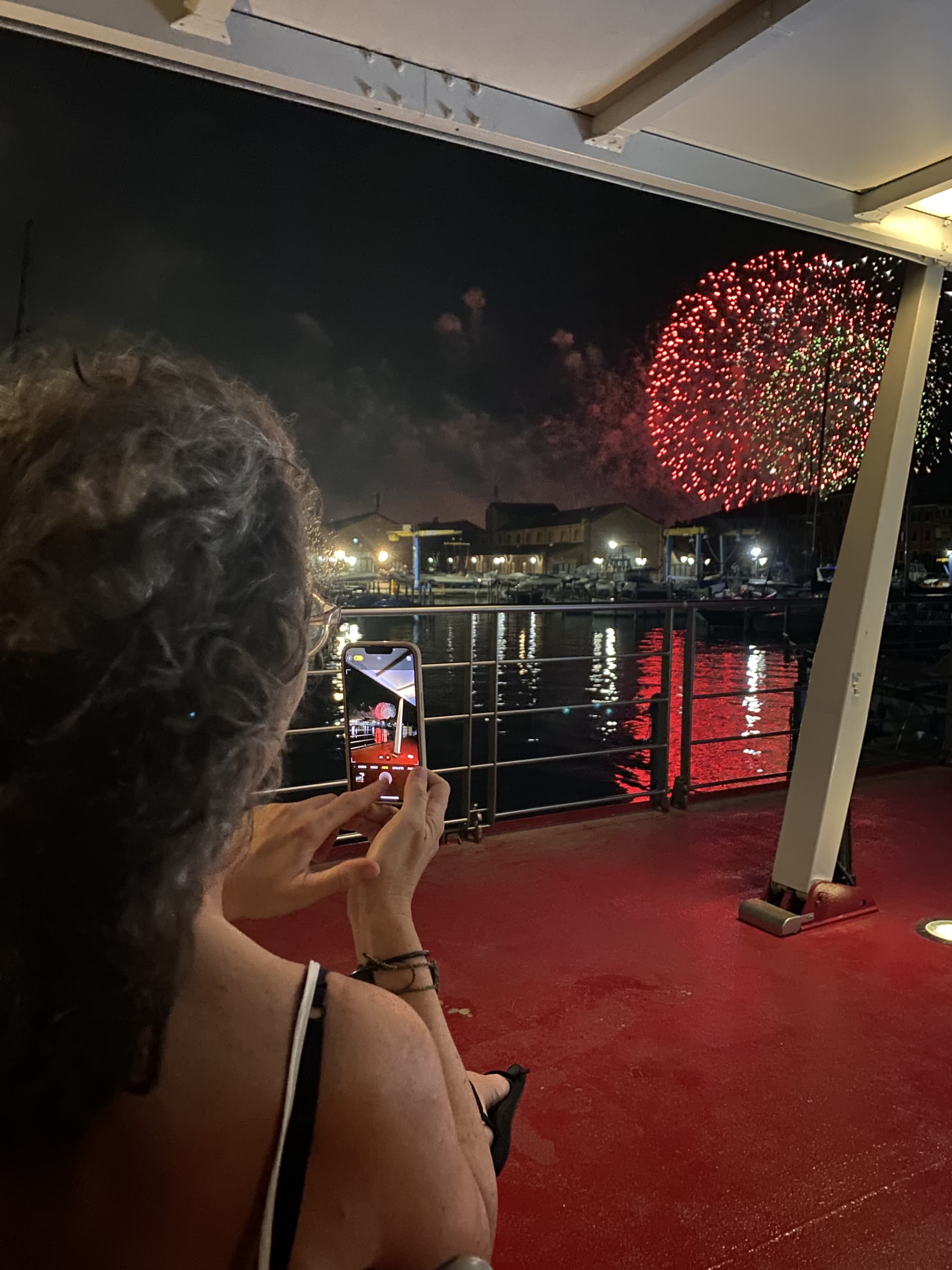 Donna che fotografa i fuochi d’artificio dal ponte di una barca durante la Festa del Redentore a Venezia